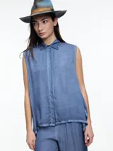 Camisa sin mangas de viscosa teñida en frío con efecto gastado, color azul deslavado. Presenta cuello clásico, cartera oculta y ruedo irregular, más largo en los laterales.
