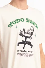 Remera de algodón color beige con estampa frontal gráfica que incluye la frase 'Todo bien' en color verde y un dibujo de una silla de oficina con texto descriptivo debajo.