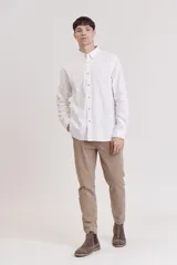 Pantalón de vestir color beige, de corte recto, con pinzas en la cintura, bolsillos laterales y traseros. Se ajusta a la cintura con cinturón de cuero marrón.