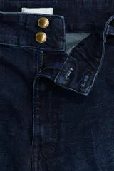 Pantalón de jean estilo wide leg con tiro alto, confeccionado en denim de algodón con leve stretch. Presenta cierre frontal con doble botón metálico, pliegues frontales y traseros, y bolsillos traseros de parche.