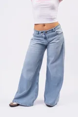 Jeans wide leg de denim rígido en lavado celeste vintage, con diseño de cintura cruzada y cierre asimétrico de doble botón.