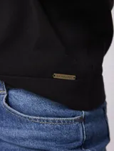 Buzo de punto fino color marrón topo, con cuello redondo y detalle de botones decorativos dorados sobre el hombro izquierdo. Presenta mangas largas con puños acanalados y una pequeña abertura lateral en los mismos.