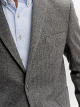 Saco de paño gris de corte regular fit, con cuello de solapa clásica, bolsillos frontales con solapa, bolsillo ojal en el pecho y cierre de dos botones.