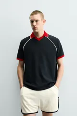 Polo de corte relajado confeccionado en tejido de algodón con estructura abierta. Presenta cuello polo con abertura frontal en V, mangas cortas tipo ranglán y acabados en rib a contraste en color rojo y blanco.