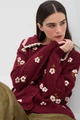 Saco de punto color bordó con bordados artesanales de flores en tonos rosados. Presenta un cuello con detalle de volados en color crema y cierre frontal con botones. De silueta amplia y cómoda.