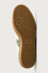 Zapatillas de estilo retro para hombre, color blanco off-white con detalles en verde oscuro y suela de goma marrón estilo gum. Presenta cordones al tono, refuerzos en gamuza en la puntera y talón, y bandas laterales verdes en contraste.