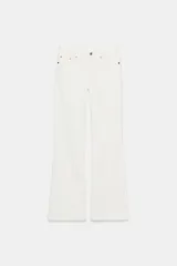 Jeans de mezclilla blancos, tiro bajo, con cinco bolsillos y cierre frontal de cremallera y botón. El corte es ajustado en muslos y se ensancha ligeramente desde la rodilla (bootcut/flare).