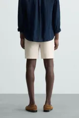 Bermuda de hombre color beige claro, corte regular fit, con pliegues frontales, bolsillos delanteros y bolsillos traseros de doble vivo con botón.