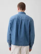 Camisa de jean de corte recto y calce relajado, con cierre frontal de botones metálicos, cuello clásico y un bolsillo frontal en el pecho.