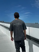 Remera gris con efecto gastado, corte oversize, mangas cortas y estampado en la espalda con el texto "SUPPLY GOODS DESIGNED IN PUNTA DEL ESTE".