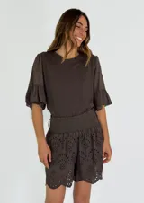Short de tiro alto color chocolate, confeccionado en tela con bordado inglés y diseño calado. Presenta una cintura elástica ancha tipo nido de abeja y ruedo con terminación festoneada.
