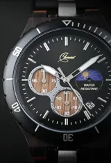 Reloj cronógrafo de la colección Imperial, con caja de madera de ébano oscuro y bisel técnico. La esfera negra presenta subdiales con textura de madera natural, indicador de fase lunar y fechador. La malla combina eslabones de acero inoxidable pulido con madera de ébano, ofreciendo un diseño sofisticado y resistente.