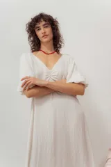 Vestido midi color blanco crudo, con escote en V, fruncido en el pecho y mangas cortas abullonadas.