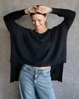 Buzo de punto negro con diseño asimétrico, más corto en la parte frontal y más largo en la parte trasera. Presenta cuello redondo, mangas largas y un corte holgado y fluido.