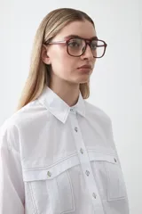 Camisa blanca de algodón con diseño utilitario y calce relajado. Presenta dos bolsillos frontales de estilo cargo con tapa y costuras a contratono.