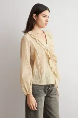 Blusa color beige de manga larga, con escote en V adornado con volados y cierre frontal con botones.