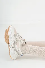 Championes chunky estilo tennis sneakers, color blanco y beige, con detalles en cuero y descarne. Incorporan un arnés desmontable con brillos y tachas, y suela de goma marrón.