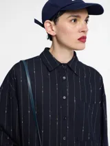 Camisa azul marino con botones en la parte delantera y bolsillo en el pecho. Diseño de rayas verticales bordadas con hilo metálico.