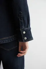 Camisa de jean de corte recto y calce holgado, con cuello clásico, cierre frontal con botones metálicos y dos bolsillos delanteros con solapa y botón.