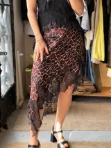 Pollera midi de satén con estampado animal print tipo jirafa en tonos burdeos, marrón y blanco, con diseño asimétrico y detalles de encaje negro en el ruedo.