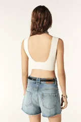 Crop top blanco de tejido de punto, con escote en V y detalle anudado en el centro del pecho, dejando una abertura en la zona abdominal. Espalda baja.