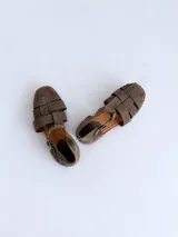 Sandalias cangrejeras de gamuza color marrón, con punta redonda, taco bajo, talonera cerrada y tira con hebilla metálica ajustable en el tobillo.