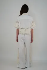 Pantalón de lino blanco con cintura elástica y cordón ajustable, de corte holgado y diseño largo, con detalles de inserciones de malla transparente con bordados florales en los laterales.