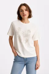 Remera de algodón de corte holgado, con cuello redondo y mangas cortas. Presenta un diseño frontal de motivos botánicos realizado con pequeños studs metálicos.