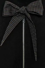 Chaqueta de punto negra con cuello redondo, cierre frontal con cremallera metálica y detalle de lazada en tejido a cuadros en contraste. Presenta mangas largas abullonadas con puños elásticos y bajo elástico.