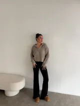 Buzo de punto grueso color gris, con cuello polo, cierre frontal parcial y capucha. Presenta un diseño de tejido acanalado con terminaciones desflecadas en el ruedo.