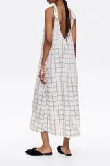 Vestido largo blanco con estampado de líneas negras formando un patrón de cuadrícula. Tiene tirantes anchos con detalle de lazo en los hombros, escote redondo pronunciado en delantero y espalda, y corte línea A.