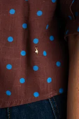 Blusa color crudo con estampado de lunares marrones, cuello camisero, cierre frontal con botones y mangas cortas holgadas.
