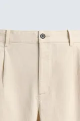 Pantalón de corte regular fit confeccionado en tejido de algodón con textura de espiga. Presenta cintura con pliegues frontales, bolsillos laterales y bolsillos traseros de vivo con botón. Cierre frontal con cremallera y botón.