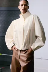 Camisa de cuello subido y manga larga con puños elásticos. Diseño holgado con cierre frontal de botones ocultos por solapa.