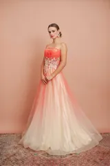 Vestido largo de fiesta, strapless, con busto drapeado y falda de tul con degradé de color coral a blanco. Presenta bordados florales en el corpiño.