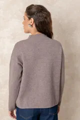 Buzo de punto color visón con cuello alto, manga larga y diseño holgado. Presenta un bordado floral en relieve al tono en la parte frontal.