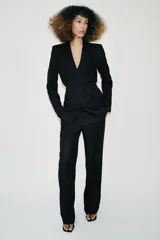 Blazer de cuello solapa y manga larga con hombreras marcadas. Presenta un diseño cruzado con cierre frontal de botones a presión, bolsillos delanteros con solapa y un detalle de cintura entallada con efecto abullonado.