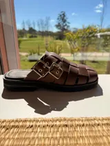 Sueco marrón de cuero trenzado con hebillas plateadas y suela de goma negra.