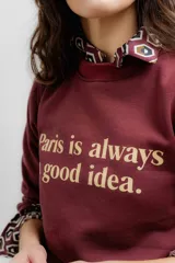 Buzo de algodón color bordó con cuello redondo, mangas largas con puños elásticos y estampa frontal con la frase 'Paris is always a good idea.' en color crema.