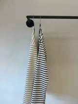 Remerón de manga larga con diseño de rayas horizontales finas en color negro sobre fondo blanco. Presenta un corte oversize, cuello redondo y un largo asimétrico con la parte trasera ligeramente más larga que la delantera.