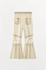 Pantalón de tiro alto con cintura elástica, confeccionado en viscosa. Presenta bolsillos de plastrón en el frente, aplicaciones de puntilla y bordados florales a tono, con bajo acabado en volantes.