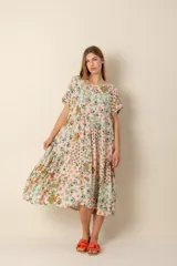 Vestido largo estampado con flores en tonos violeta, naranja, verde y azul sobre un fondo beige claro. Tiene cuello en V y mangas cortas.