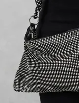 Cartera de strass color negro, con cierre metálico y bolsillo interior. Incluye una correa de mano trenzada y un cierre de cremallera.