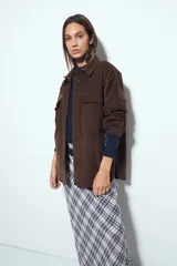 Sobrecamisa de pana color marrón oscuro, con diseño de corte amplio, cuello camisero, cierre frontal con botones y bolsillos con solapa en el pecho.
