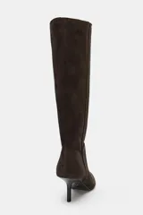 Bota de caña alta confeccionada en serraje, con diseño de punta fina y tacón fino. Presenta detalle de pespuntes en el cuerpo y sistema de calce pull-on.