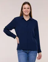 Camisa blanca de corte clásico y caída fluida, con cuello camisero tradicional, abotonadura frontal oculta y mangas largas con puños anchos.