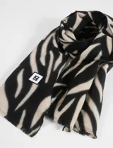 Bufanda rectangular con estampado animal print de cebra en blanco y negro, con detalle de etiqueta cuadrada con logo en el extremo inferior.