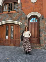 Pollera midi de corte amplio con estampado escocés en tonos marrones. Presenta un diseño distintivo con un detalle de atado en la cintura que simula puños de camisa y cierre frontal con botones.