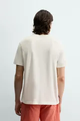 Camiseta de corte regular, color crudo, con cuello redondo y manga corta. Presenta un estampado frontal con diseño circular en tono rojizo con efecto lavado.