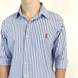 Camisa de vestir a rayas verticales azules y blancas, de corte clásico, con cuello italiano y mangas largas con puños abotonados. Presenta logo bordado en el pecho. Marca Duxon.